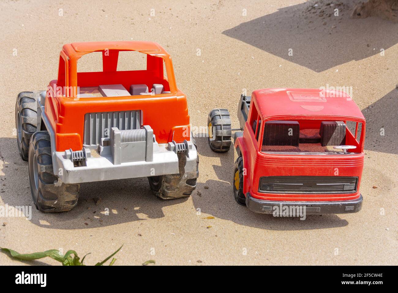 Zwei Kinder`s Spielzeugautos, aus Vorbesitz, gebrochen stehen auf dem Sand unter der hellen Sommersonne Stockfoto